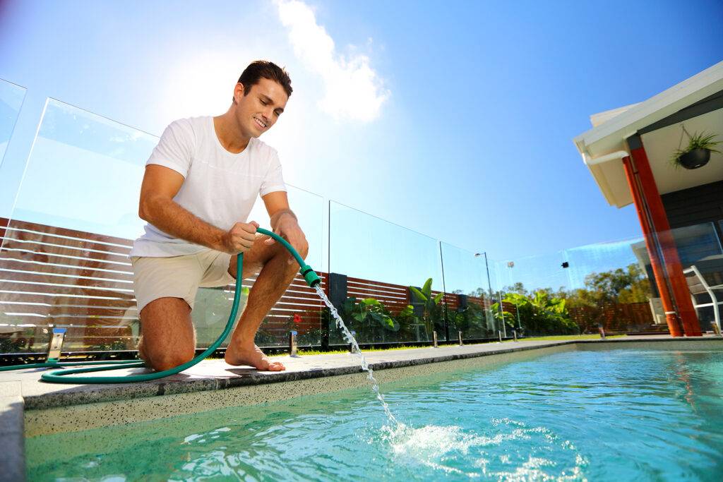 man filling up pool with water hose